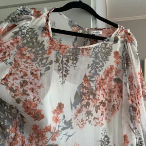 Blommig långklänning med puffärmar - Säljer en romantisk långklänning med blommigt mönster i korall, grått och rosa på vit botten. Klänningen har rund halsringning och långa puffärmar. Tunt, luftigt material som ger en flowy känsla. Perfekt för sommarens tillfällen.