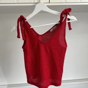 Röd stickad linnetopp från Mango - Säljer en röd stickad linnetopp från Mango med knytband på axlarna. Toppen är ärmlös och har en luftig, lite transparent struktur. Perfekt för varma dagar eller som ett snyggt lagerplagg.