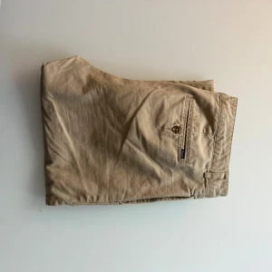 Beiga chinos från Polo Ralph Lauren - Säljer ett par klassiska beiga chinos från Polo Ralph Lauren. Byxorna har normal passform, raka ben och är tillverkade i mjuk bomull. Perfekta för en stilren och avslappnad look. Fickor bak med knapp och diskret logga. Byxorna passar en person från 170 till 175 ganska slim fit öppen till bud 