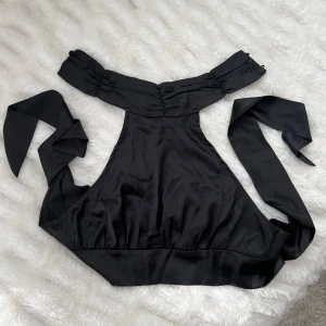 Svart halterneck topp  - Säljer en svart halterneck topp från SHEIN i glansigt material. Toppen har hög hals med knappar i nacken och knytning i ryggen. En knapp har tyvärr ramlat av, annars är den i väldigt fint skick och knappt använd. 