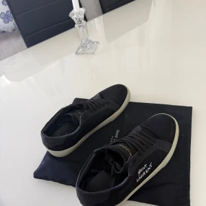Saint Laurent skor  - Svarta sneakers från Saint Laurent med vit sula och snörning. Skorna har en klassisk låg modell med Saint Laurent-logga broderad på sidan. Perfekta för en stilren och trendig look.
