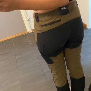 Gröna och svarta friluftsbyxor från CRIW - Säljer ett par gröna och svarta friluftsbyxor från CRIW med flera praktiska fickor och dragkedjor. Materialet känns slitstarkt och bekvämt.