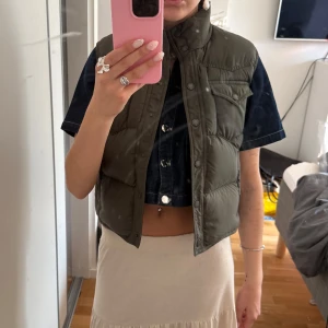 Olivgrön croppad dunväst från Ralph Lauren - Säljer en olivgrön croppad dunväst från Ralph Lauren. Västen har tryckknappar framtill och en hög krage. Knappt använd! Storlek M men liten i storlek, passar mig som har xs/s