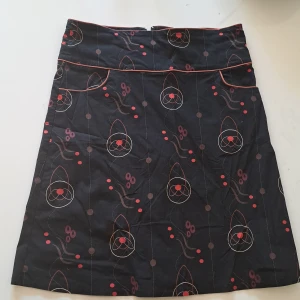 Svart kjol med grafiskt mönster - Säljer en svart kjol med mönster i orange, rött och brunt. Den har ett ifyllt slitt och dradkedja i bak och fickor framtill. Midjemått 39 cm. Skriv gärna vid funderingar🙂