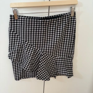 Svartvit rutig kjol med volang - Säljer en svartvit rutig kjol med volangdetalj nertill. Kjolen har en rak passform och är kort i modellen. Perfekt för dig som gillar klassiska mönster med en twist.