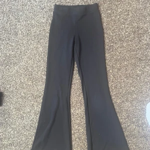 Svarta utsvängda byxor från Gina Tricot - Säljer ett par svarta utsvängda byxor från Gina Tricot i storlek XXS. Byxorna har hög midja och är tillverkade i ett stretchigt material som sitter skönt. Perfekta för dig som gillar en trendig och bekväm stil. (byxorna är bara 92cm lång, passar för en tjej som är typ från 152cm lång till ca 160cm lång) (har inte använt)