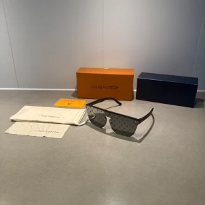 Svarta LV glasögon  - Stilrena svarta solglasögon från Louis Vuitton med LV-monogram på glasen. Rektangulär form och breda skalmar i svart plast. Kommer med originalfodral, putsduk och ask. Perfekt accessoar för dig som vill sticka ut med lyxig design.