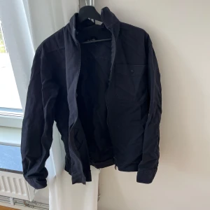 Svart jacka från Selected Homme - Säljer en svart jacka från Selected Homme med klassisk krage och knappstängning vid ärmslut. Jackan har en bröstficka med knapp och enkel, stilren design. Perfekt för dig som gillar minimalistisk stil.