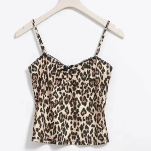 Leopardmönstrad linnetopp med spetsdetalj - Trendig linnetopp med leopardmönster och tunna axelband. Toppen har en liten rosettdetalj framtill och spetskant längs urringningen. Perfekt för att skapa en cool och djärv look.