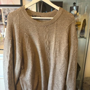 Ljusbrun stickad tröja från Lager 157 - Mysig beige stickad tröja från 157 med diskret kabelstickat mönster framtill. Tröjan har rund halsringning och långa ärmar, perfekt för kyligare dagar. Ser tyvärr mer gul ut på dessa bilder än i verklighet.