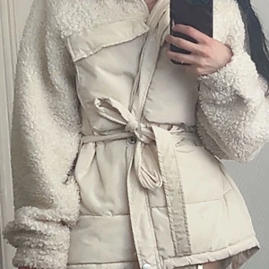 Beige teddyjacka med bälte från Pieces - Säljer en beige teddyjacka från Pieces med puffer-detaljer och knytbälte i midjan. Jackan har långa ärmar i teddy-material och dragkedja framtill. Perfekt för dig som vill ha en mysig och trendig look. Sitter jättefint på kroppen. Passar till storlek 32-34