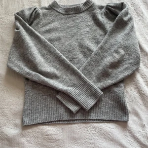 Grå stickad tröja med puffärmar - Mysig grå stickad tröja med puffdetaljer vid axlarna och ribbade muddar vid ärmslut och nederkant. 🩶