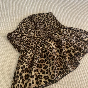 Leopardmönstrad tubtopp - Säljer en leopardmönstrad tubtopp. Med smockad överdel och volangig nederdel. Toppen är axelbandslös och har en snygg, figurnära passform upptill. Den är strechig. 