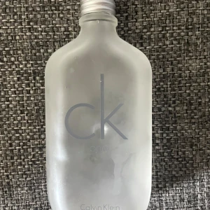 CK One Eau de Toilette från Calvin Klein - Halva kvar!! Säljer en klassisk CK One parfym från Calvin Klein. Flaskan är i frostat glas med minimalistisk design och silverfärgad skruvkork. Doften är unisex och fräsch, perfekt för dig som gillar rena och lätta toner.
