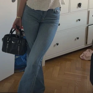 Ljusblå bootcut jeans - Säljer ett par ljusblå bootcut jeans med klassisk femficksdesign och låg midja. Jeansen har en snygg passform som sitter tajt upptill och släpper ut vid benen. Perfekta till vardags och lätta att matcha med olika toppar.
