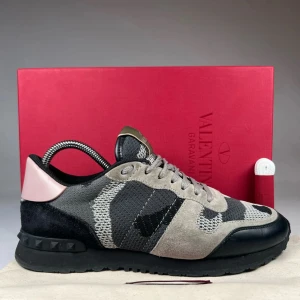 Valentino Rockrunner sneakers i grå och svart - Säljer ett par Valentino Rockrunner sneakers med grått och svart camouflage-mönster, detaljer i mocka och skinn samt en rosa häl. Skorna har snörning, svart sula och klassisk rund tå. Perfekta för dig som gillar exklusiva och unika sneakers.