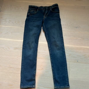 Blå jeans från J.Lindeberg - Säljer ett par klassiska blå jeans från J.Lindeberg med normal passform och raka ben. Jeansen har fem fickor, gylf med dragkedja och snygga kontrastsömmar. Perfekta till vardags och enkla att matcha med olika stilar.