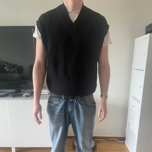 Svart stickad väst med v-ringning - Snygg svart stickad väst med v-ringning. Perfekt att bära över en t-shirt eller skjorta för en stilren look. Västen har en klassisk passform och ribbade kanter vid ärmhål och nederkant. Hör av er vid frågor och funderingar! 