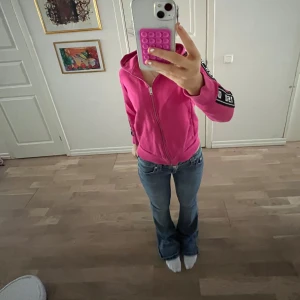 Rosa hoodie från Diesel - Säljer en snygg rosa hoodie från Diesel med dragkedja och huva. Tröjan har långa ärmar och svarta detaljer med Diesel-logga längs ärmarna. Perfekt för en avslappnad stil.