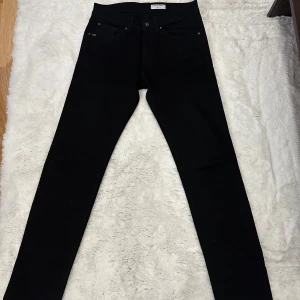 HELT NYA Svarta jeansbyxor från Tiger of Sweden - Snygga svarta jeansbyxor från Tiger of Sweden med klassisk femficksdesign och raka ben. Byxorna har en stilren look och passar perfekt till många olika outfits. Märkespatch bak i midjan och knappgylf framtill.
