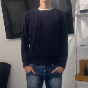 Gant Crewneck - Säljer en stilren NavyBlue ribbad tröja från Gant med rund halsringning. Tröjan har en diskret och stilren logga på bröstet perfekt för kyligare dagar Storlek S