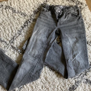 Grå jeansbyxor med dekorativa sömmar - Säljer ett par grå jeansbyxor med snygga, markerade vita sömmar och ficklock med knapp bak. Klassisk femficksmodell och normal passform. Perfekta till vardags för en avslappnad men ändå stilren look. En liten slitning lägst ner på byxorna men det syns knappt 