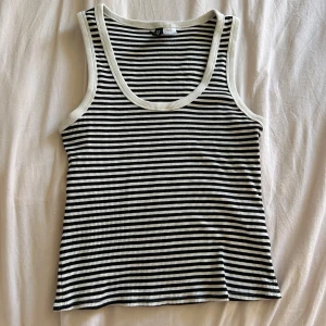 Randig ribbad linnetopp - Säljer en svartvit randig ribbad linnetopp med breda axelband och rundad halsringning. Perfekt för varma dagar och enkel att matcha med jeans eller shorts. Bara använd 1 gång