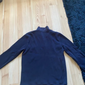 Mörkblå tröja med halv dragkedja från Polo Ralph Lauren - Säljer en mörkblå tröja från Polo Ralph Lauren med halv dragkedja och klassisk krage. Tröjan har lång ärm och en liten röd broderad logga på bröstet. Perfekt för en stilren och avslappnad look. Pris ej hugget i sten