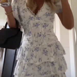 Vit blommig volangklänning med v-ringning - Superfin kortklänning i vit med blått blommönster och v-ringad hals. Klänningen har volanger i kjolen och puffärmar. Perfekt för sommarens alla tillfällen. Materialet känns lätt och luftigt. Storlek M men sitter som en xs! Så liten i storlken!!💗🌸