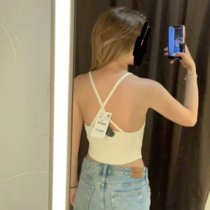 Vit ribbad croppad linnetopp med knyt - Säljer en vit croppad linnetopp med smala axelband och ribbad struktur. Toppen har en snygg v-ringning och knyt framtill som jag tagit bort. Perfekt till jeans eller shorts i sommar! Köpt för 280 säljer för 100, använd endast 1 gång.