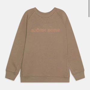 Beige sweatshirt från Björn Borg - Säljer en beige sweatshirt från Björn Borg med tryckt logga i ljusrosa framtill. Tröjan har rund halsringning och långa ärmar. Perfekt för en avslappnad och stilren look.