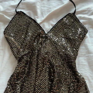 Svart paljetttröja med smala knytband - Säljer en svart tröja med guld paljetter över hela tröjan, tröjan är v ringad och har en dragkedja bak på ryggen som inte syns när den är stängd. Tröjan är aldrig använd för att jag helt enkelt hade glömt att den existerade.❤️