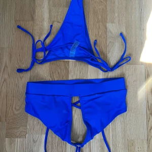 Blå bikini med knyt och hög midja - Säljer en snygg blå bikini med trekantsöverdel och knyt i sidorna. Underdelen har hög midja och dekorativ snörning framtill. Perfekt för stranden eller poolen!