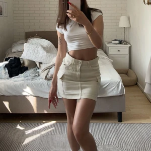 Beige minikjol med fickor - Snygg beige minikjol med stora fickor framtill. Kjolen har en rak passform och är perfekt för en trendig vardagslook. Passar till crop tops och sneakers.