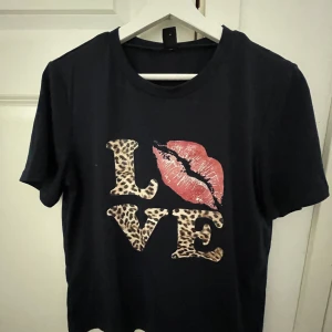 Svart t-shirt med leopardmönstrad LOVE-tryck - Svart t-shirt som passar vem som helst går bra att styla till mycket!! Fint skick aldrig använd vet ej vart den är ifrån då de är en present!! Skriv om ni har någon fråga eller om ni vill diskutera priset!!