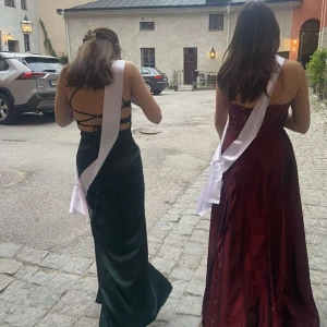 Mörkgrön balklänning med fin rygg - Säljer en mörkgrön lång balklänning med smala axelband och jätte fin rygg där banden korsar vrn. Klänningen har figurnära passform och snygga banddetaljer i ryggen, och även en slits på framsidan av klänningen. Perfekt för bal. Passar xs och S.