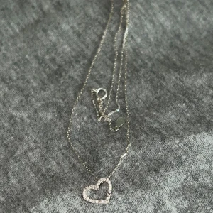 Halsband i silver med hjärthänge - Säljer ett tunt halsband i silver från Glitter med ett glittrigt hjärthänge. Finns lite defekter på hjärtat som man kan se i sista bilden men annars i fint skick. 