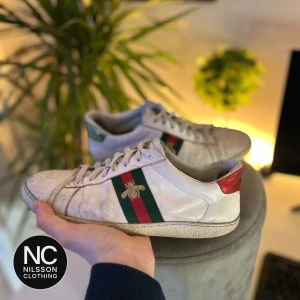 GG skor  - Snygga vita GG skor med klassiska ränder i blått och rött samt ett broderat bi på sidan. Skorna har snörning och en färgglad detalj på hälen i rött och blått. Finns kvitto