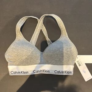 Grå bh från Calvin Klein - Säljer en grå bh från Calvin Klein med vit resår och svart logotyp runt om. Den är helt ny med prislapp och ALDRIG ANVÄND! 