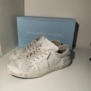 Vita sneakers från Philippe Model - Säljer ett par klassiska vita sneakers från Philippe Model Paris. Skorna har rund tå, platt sula och är tillverkade i skinn med snygga detaljer och snörning framtill. Perfekta för dig som gillar stilrena och tidlösa sneakers. Vid snabb affär går priset att diskutera