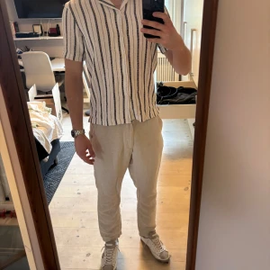 Vit kortärmad skjorta  - Säljer en fräsch vit skjorta med korta ärmar och vertikala svarta ränder. Skjortan har klassisk krage och knäppning framtill. Perfekt för en avslappnad och stilren look. Köptes från Zara för drygt 700kr. Nyskick 10/10. Storlek s/m 