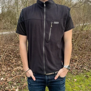 Svart fleeceväst från Peak Performance - Säljer en svart fleeceväst från Peak Performance med dragkedja framtill. Västen har en hög krage och en diskret logga på bröstet. Perfekt för lager-på-lager under kyliga dagar. Modellen är 180 cm