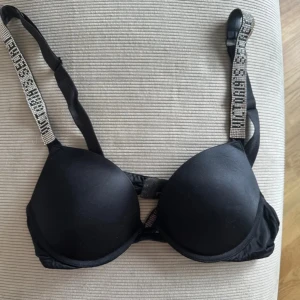 Svart bh med glittriga axelband - Snygg svart push-up bh med vadderade kupor och glittriga axelband som ger en extra touch. Perfekt för att känna sig både bekväm och stilren. Axelbanden är justerbara för bästa passform och lite små defekter därav priset. Bilden är från tidigare ägare. 