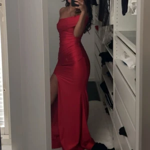 Röd one shoulder festklänning - Säljer en fantastisk röd långklänning i axelbandslös stil i storlek S som är köpt från USA och märket är populärt där. Klänningen har en tight passformen är stretchig och framhäver figuren och är perfekt för festliga tillfällen. Kan passa storlek Xs S och möjligtvis M. Materialet är mjukt tjockt satin och, vilket ger en elegant look. Perfekt för festliga tillfällen! Använd endast 1 gång i få timmar. Kontakta för diskutin om pris eller fler frågor! 