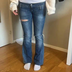 Blå bootcut jeans med slitningar - Snygga blå bootcut jeans med slitningar på knäna. De har en klassisk femficksdesign och låg midja. Perfekta för en avslappnad stil. MÅTT 39CM rakt över. 75cm innerbenslängd. Jag är 166 och de sitter som de sitter på bilden på mig❣️