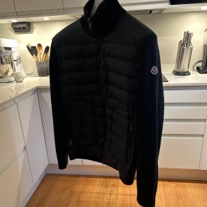  Moncler cardigan  - Säljer en stilren svart jacka från Moncler. Jackan har en quiltad design med dragkedja framtill och långa ärmar. En klassisk och tidlös modell som passar till det mesta. 8,5/10 skick, kvitto allt medföljer.. Köpt på NK 2024💪🏻 Nypris 10 000!