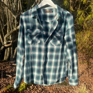 Flannelskjorta från Lee - Säljer en snygg rutig skjorta från Lee i grönt, blått och vitt. Skjortan har långa ärmar och två bröstfickor med knappar. Perfekt för en avslappnad stil.