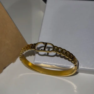 Guldarmband med kedjedetalj - Elegant guldarmband med en stilren kedjedesign och en dekorativ detalj i mitten. Helt oanvänd och ny. Materialet är rostfritt stål med 18K guldplätering. 