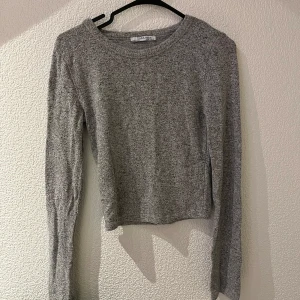 Grå stickad tröja från Zara - Säljer en stilren grå stickad tröja från Zara. Tröjan har en klassisk rund hals och långa ärmar, perfekt för kyligare dagar. Den är mjuk och bekväm, idealisk för en avslappnad look. Passar bra till jeans eller kjol.