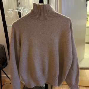 Beige stickad polotröja - Säljer en mysig beige stickad polotröja med hög krage. Tröjan har långa ärmar och ribbade muddar vid ärmslut och nederkant.